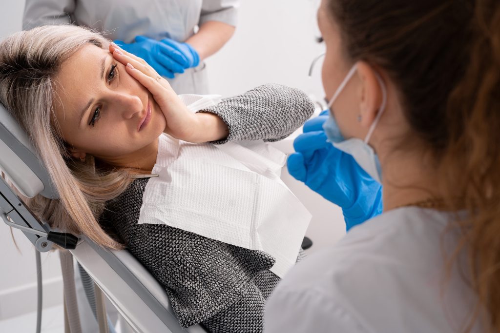 beautiful caucasian girl with toothache sits in a dental chair. Professional dentist helps his female patient in pain, emergency dental
