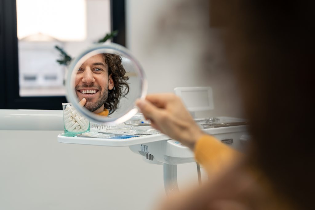 man looking into a mirror, showing his new dental implants