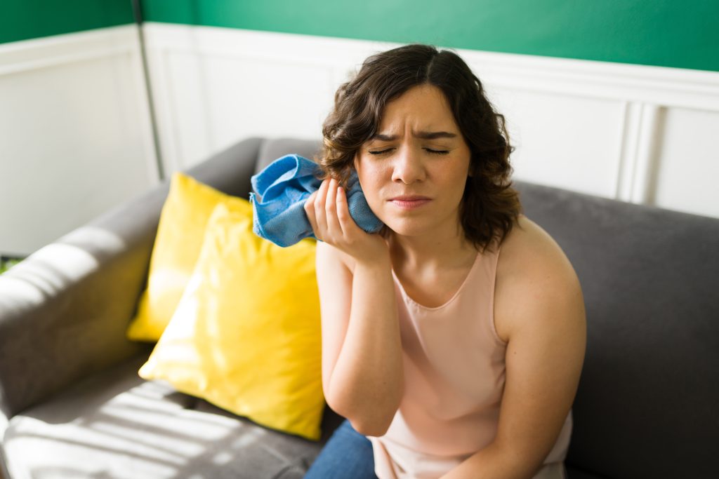 Stressed woman having a lot of pain and putting a compress on her face, knocked out tooth