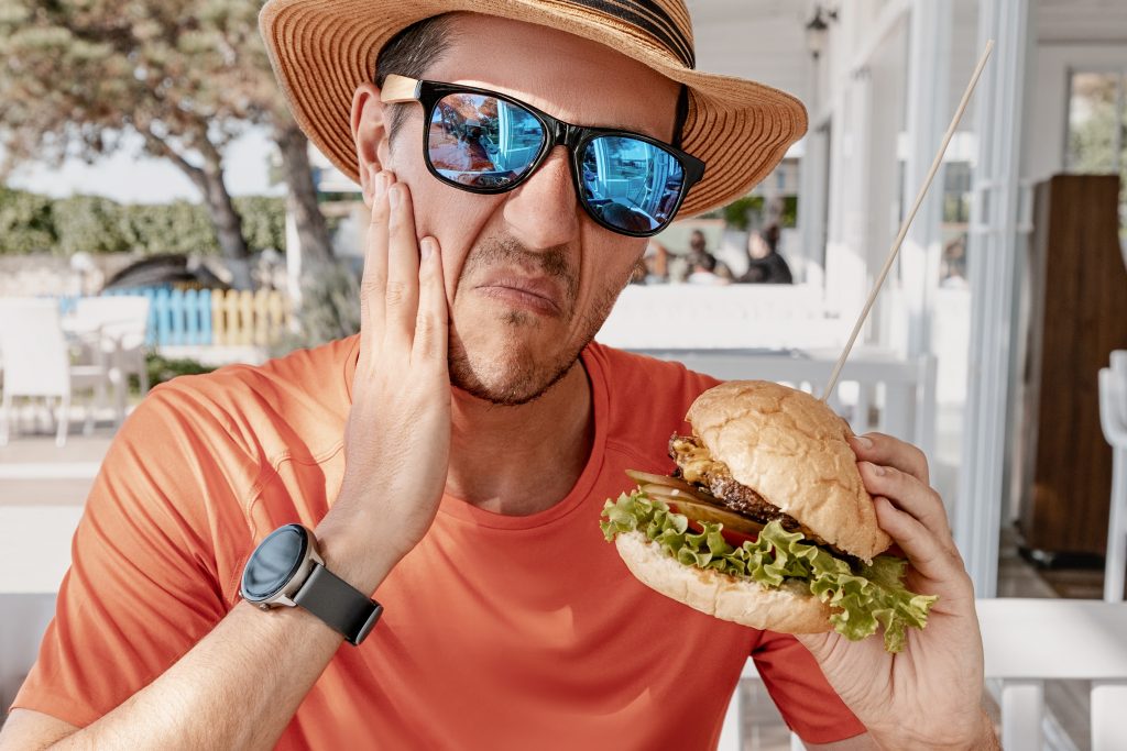 man biting down on a burger in pain, damaged filling